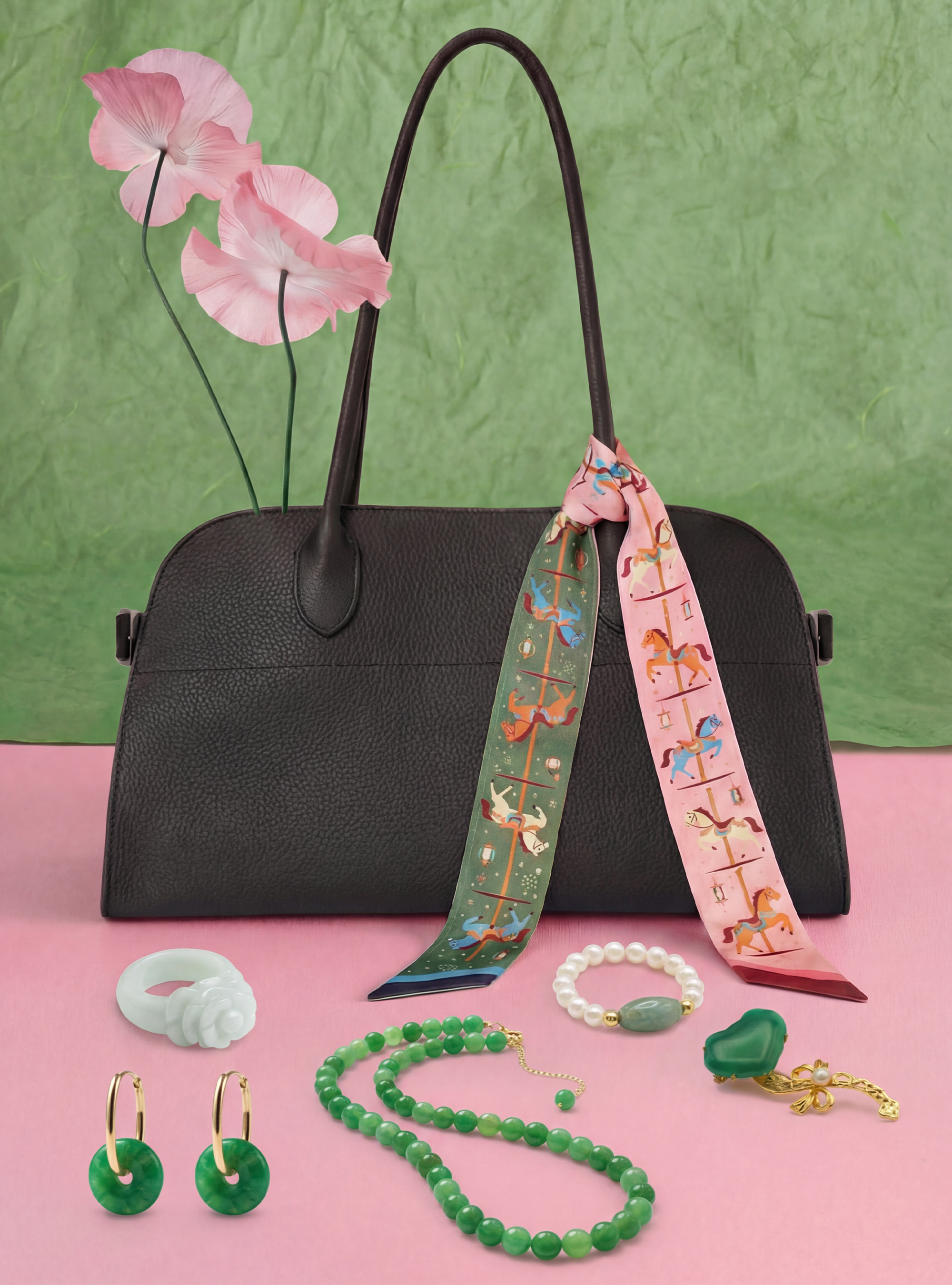 Black handbag with colorful twilly, jewelry, and flowers on a pink and green background
