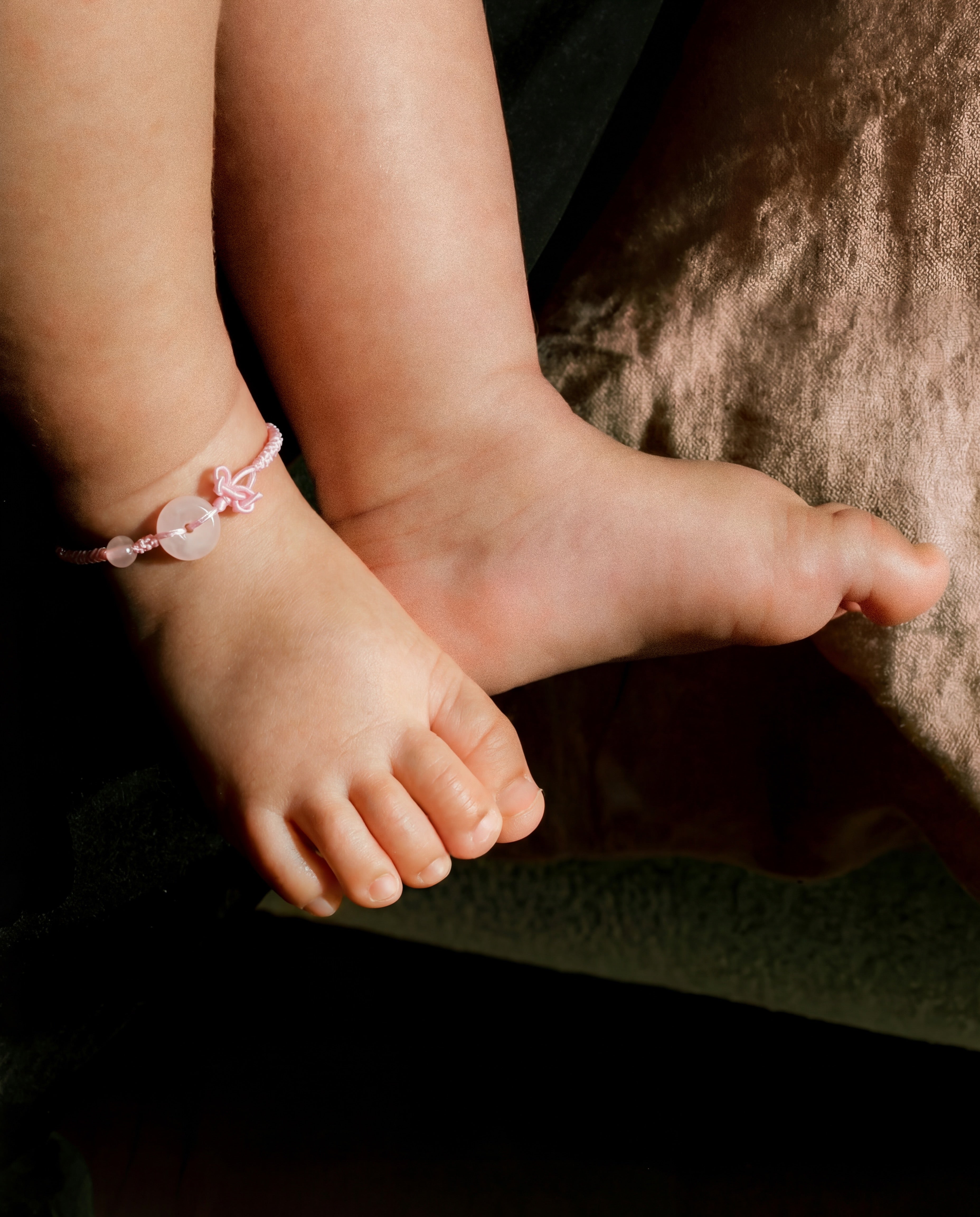 Close-up of a child's feet with a pink anklet on a dark background