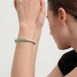 Woman wearing a green and silver beaded bracelet on a plain background