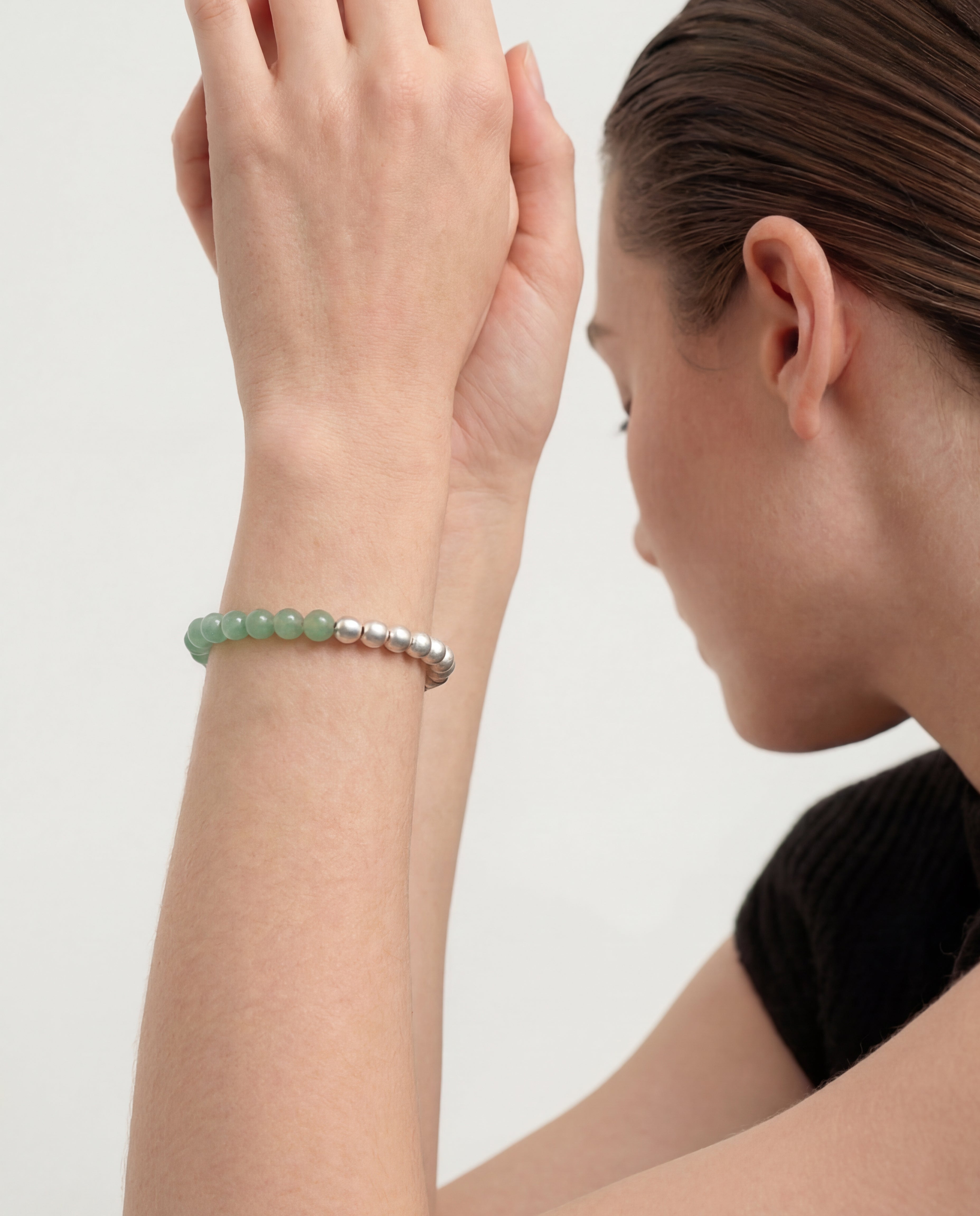 Woman wearing a green and silver beaded bracelet on a plain background