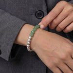 Person wearing a bracelet with green and silver beads on a gray coat background
