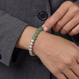 Person wearing a bracelet with green and silver beads on a gray coat background