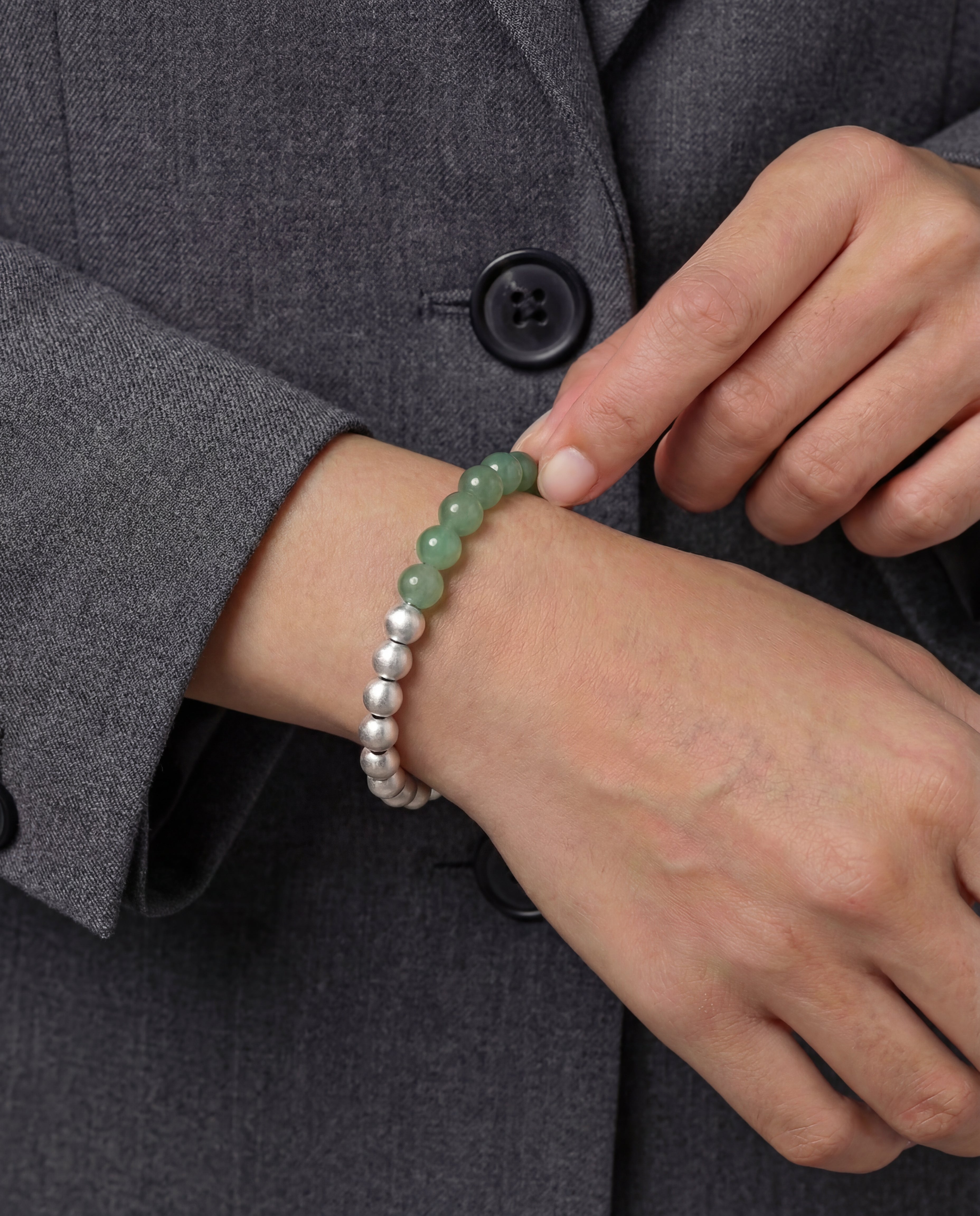 Person wearing a bracelet with green and silver beads on a gray coat background