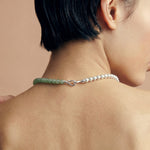 Close-up of a person wearing a necklace featuring silver and green beads on a beige background