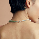 Close-up of a person wearing a necklace featuring silver and green beads on a beige background