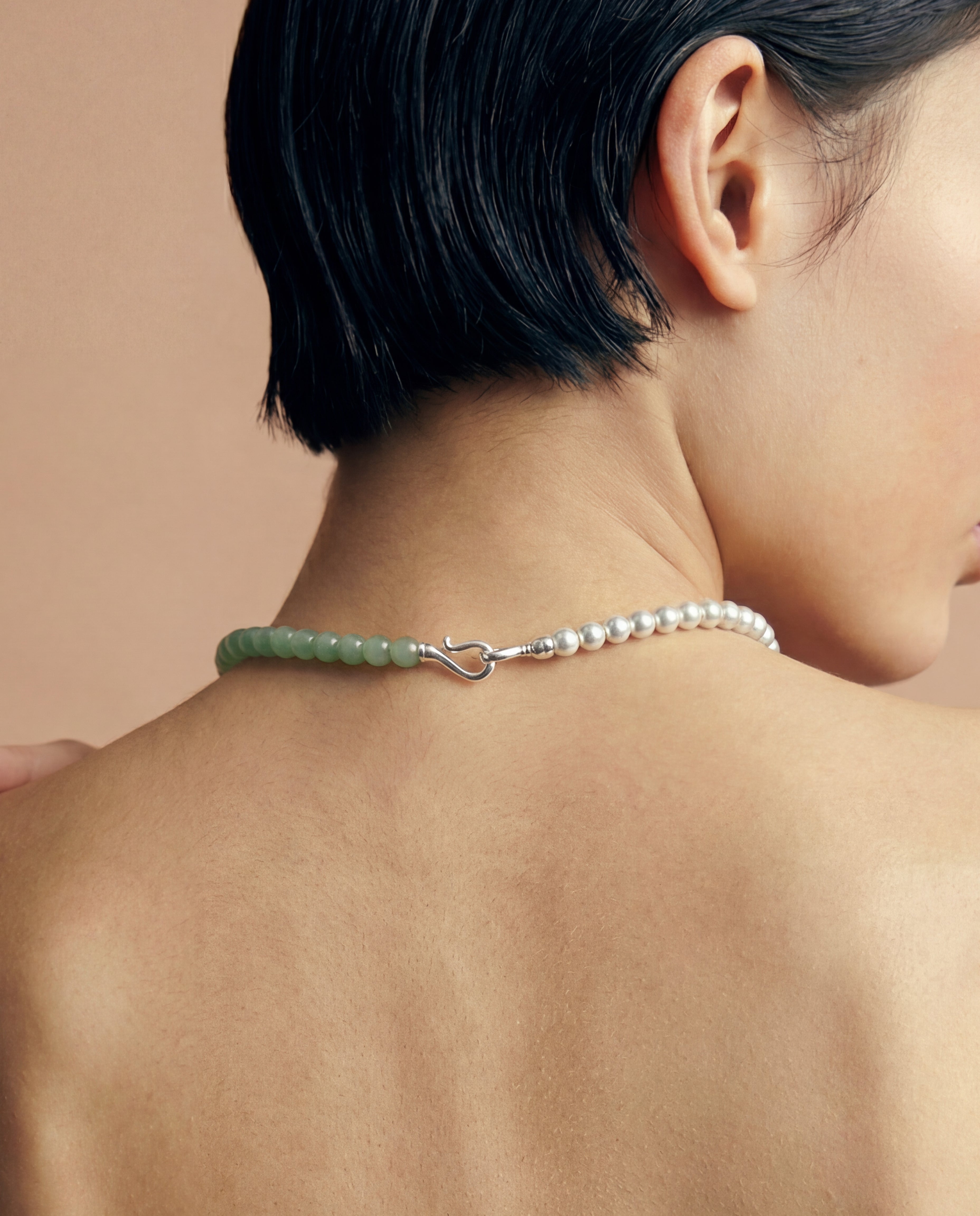 Close-up of a person wearing a necklace featuring silver and green beads on a beige background