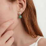 Close-up of a person wearing a green drop earring with a white background