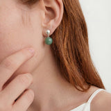 Close-up of a person wearing a green drop earring with a white background