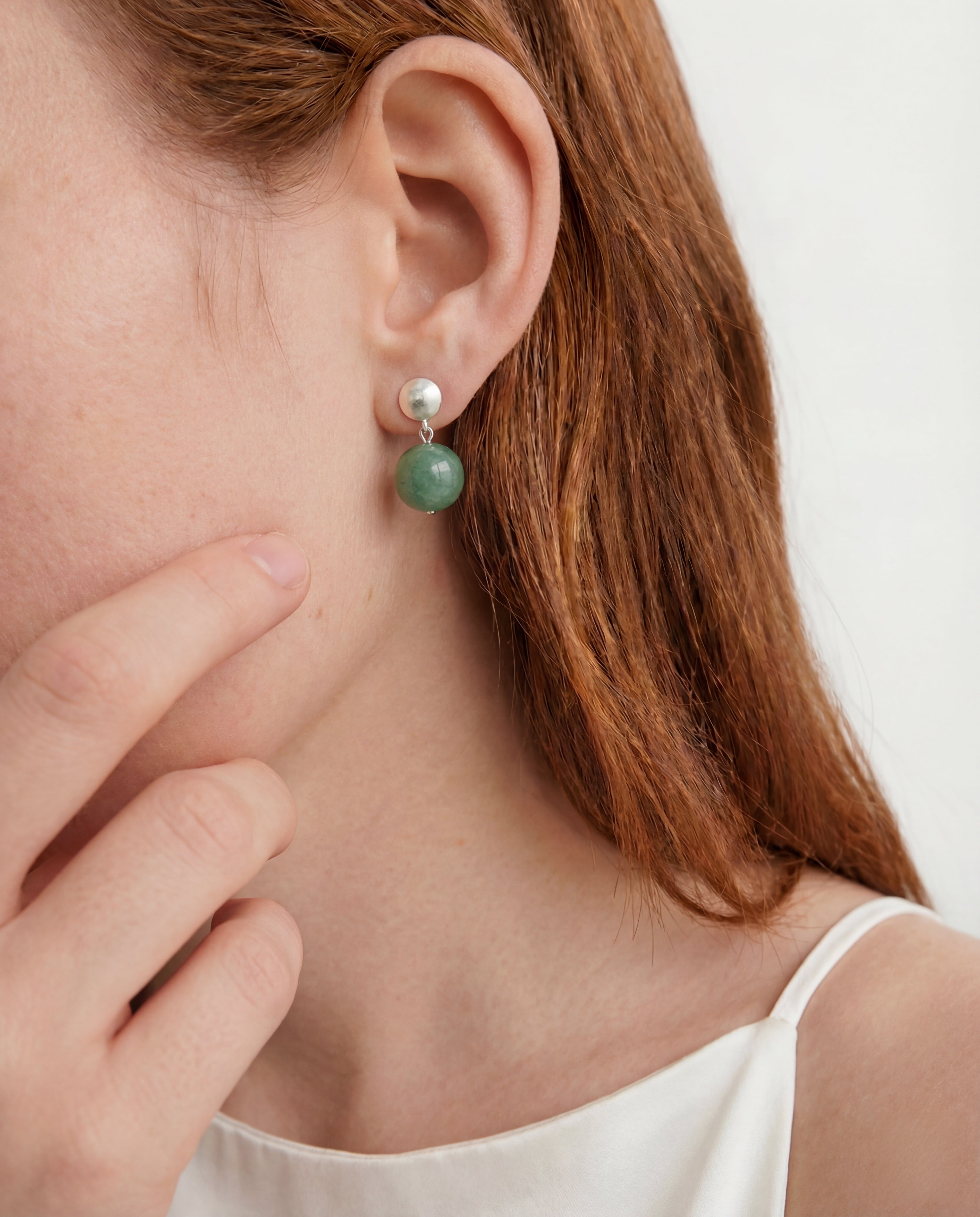 Close-up of a person wearing a green drop earring with a white background