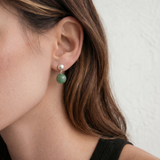 Close-up of a person wearing a green and silver earring against a neutral background