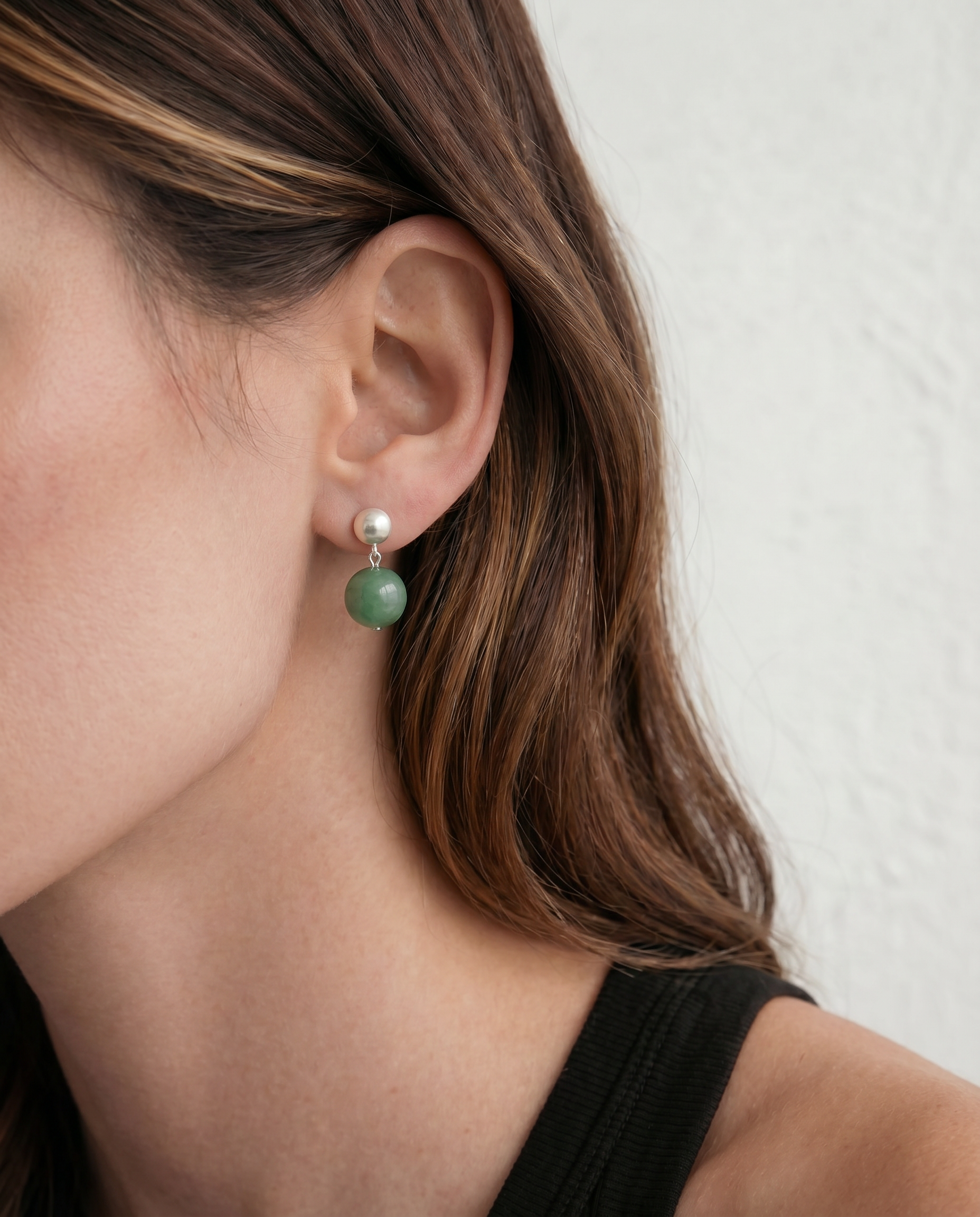 Close-up of a person wearing a green and silver earring against a neutral background