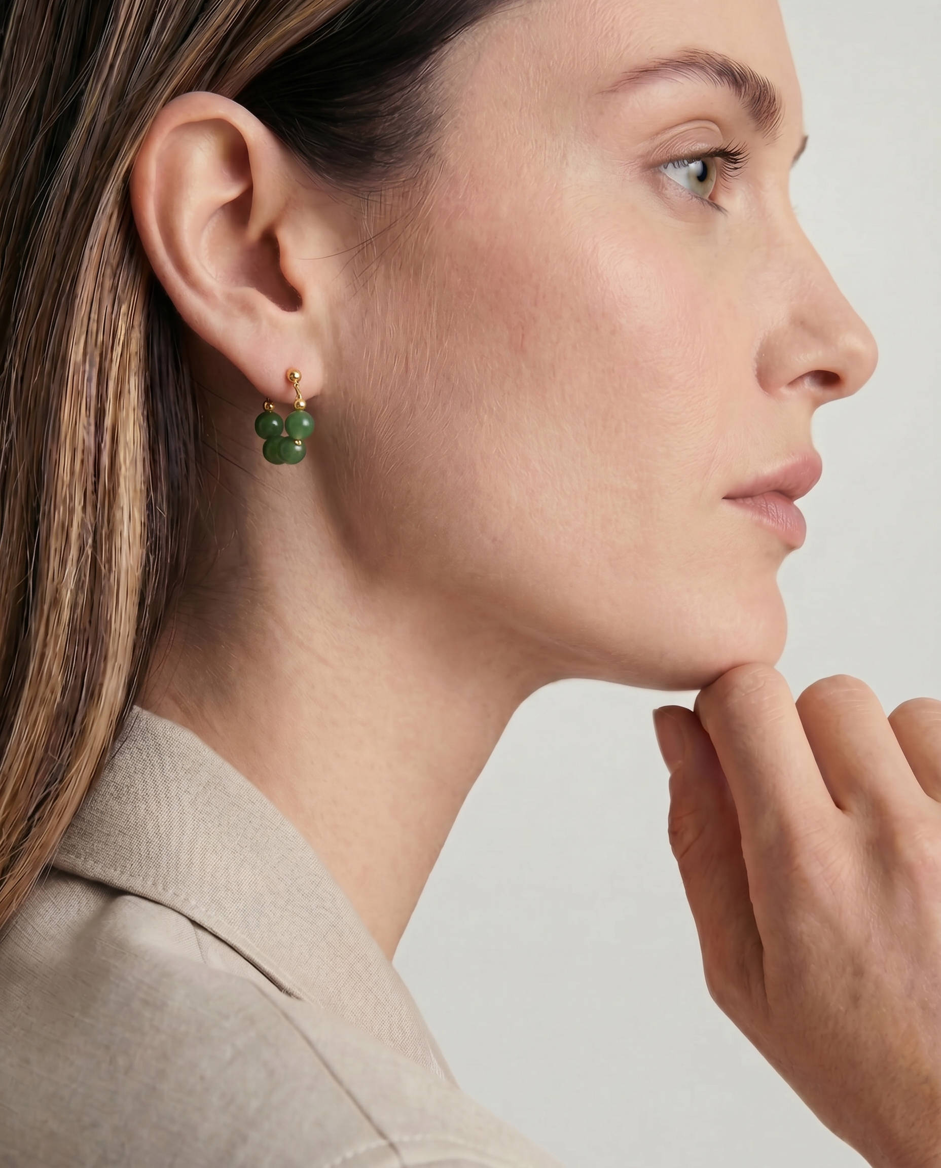 Close-up of a woman wearing green beaded hoop earrings with a neutral background