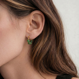 Close-up of a person wearing green beaded earrings with gold hooks.