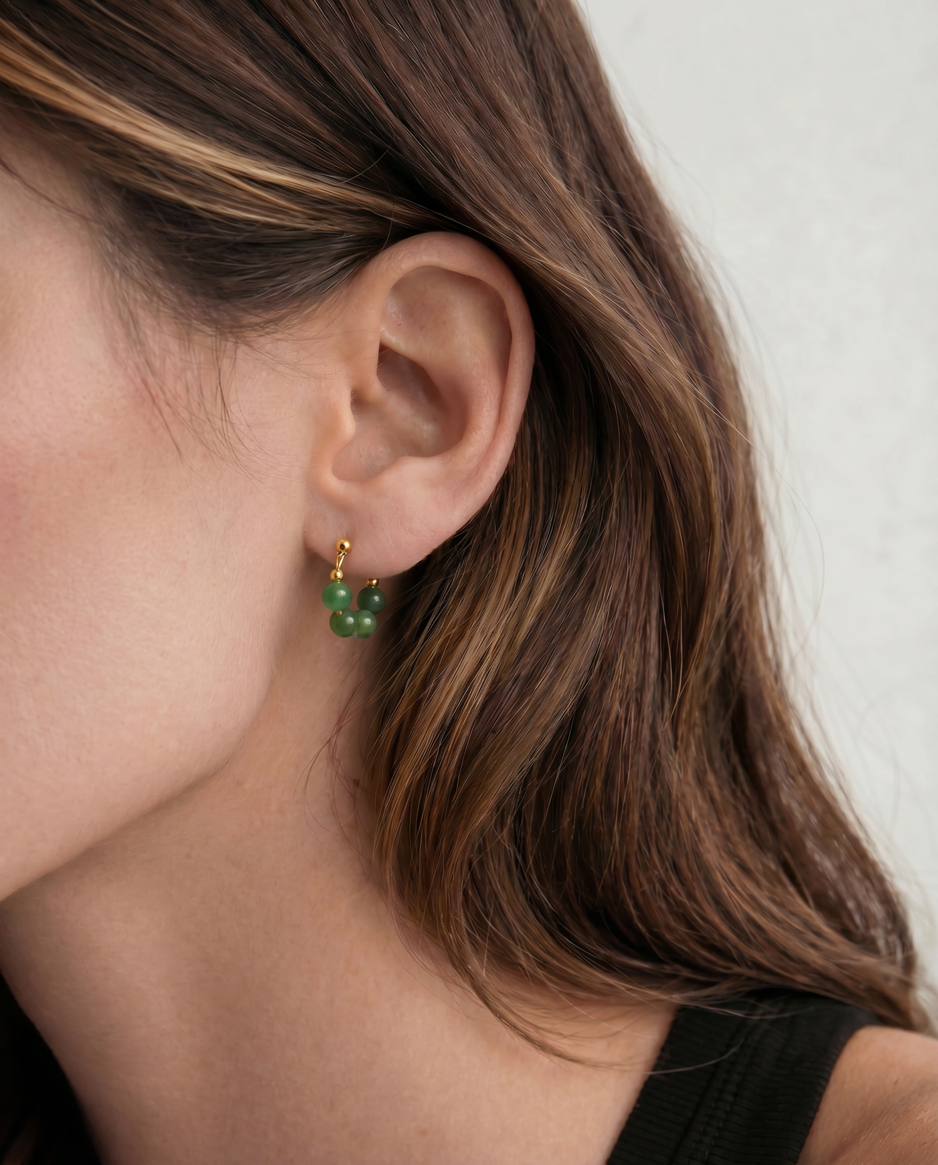 Close-up of a person wearing green beaded earrings with gold hooks.