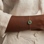 Person wearing a gold bracelet with a green stone on a neutral background