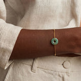 Person wearing a gold bracelet with a green stone on a neutral background