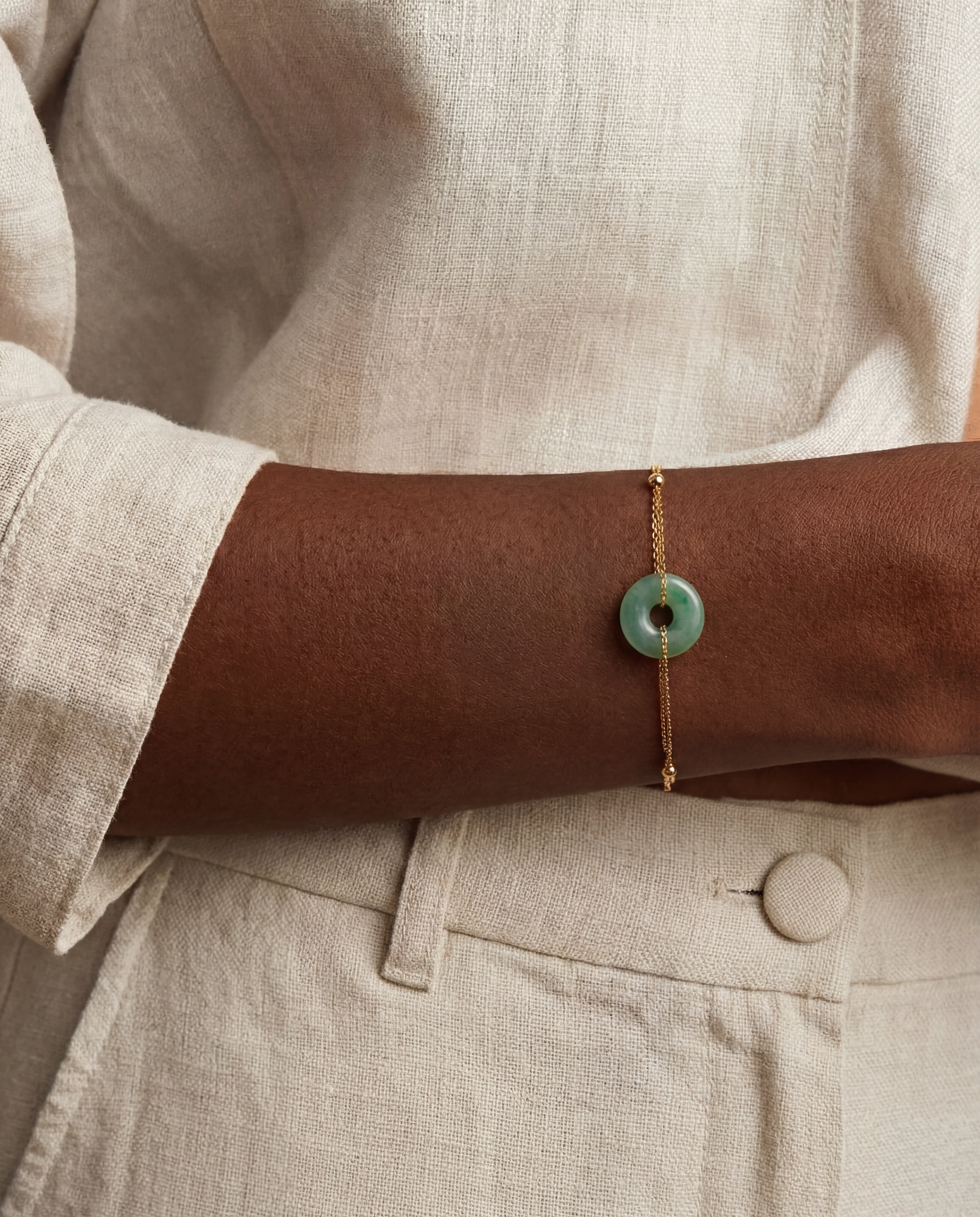Person wearing a gold bracelet with a green stone on a neutral background