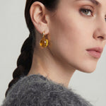 Close-up of a woman wearing a gold gemstone earring with a gray fur collar on a light background