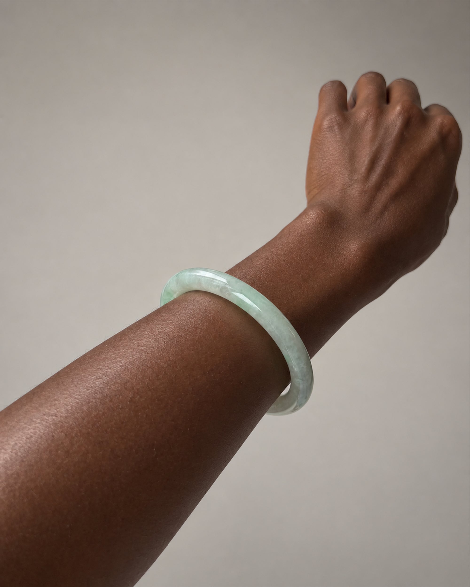 A light green jadeite bangle bracelet worn on a person's wrist, shown against a plain neutral background.
