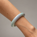 A light green and lavender jadeite bangle bracelet worn on a person's wrist, shown against a neutral gray background.