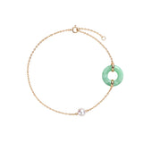 A delicate gold chain bracelet featuring a light green jadeite ring pendant and a single white pearl bead, displayed on a clean white background.