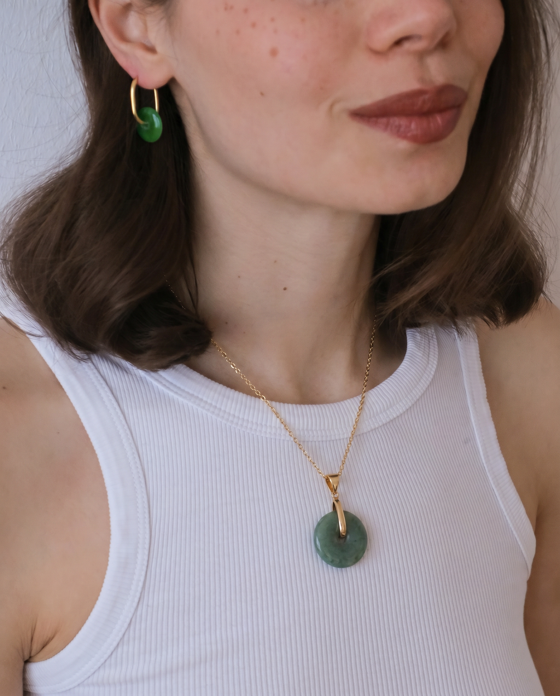 Woman wearing a gold necklace with a green pendant against a neutral background