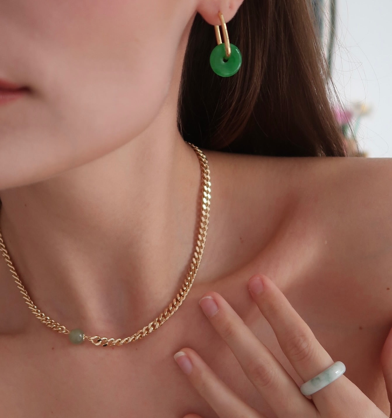 Close-up of a person wearing gold chain necklace and green hoop earrings.