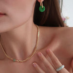 Close-up of a person wearing gold chain necklace and green hoop earrings.