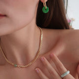 Close-up of a person wearing gold chain necklace and green hoop earrings.