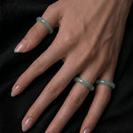 Hand wearing three green jade rings on a black background