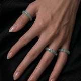 Hand wearing three green jade rings on a black background