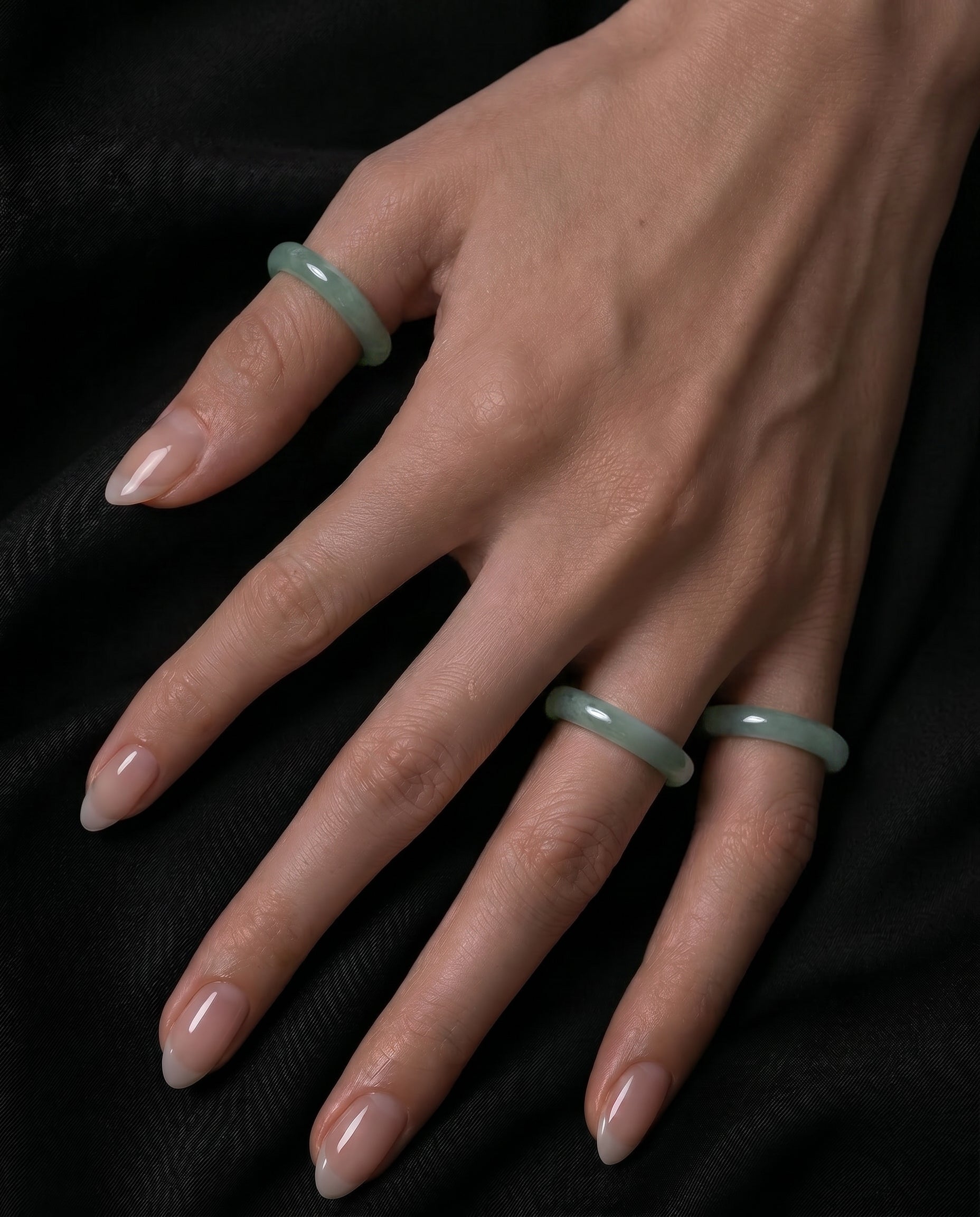 Hand wearing three green jade rings on a black background