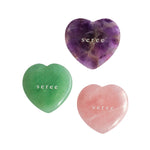 Three polished heart-shaped crystal stones on a white background: a purple amethyst, a green jade, and a pink rose quartz, each engraved with the name 'seree'.
