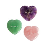 Three polished heart-shaped crystal stones on a white background: a purple amethyst, a green jade, and a pink rose quartz, each engraved with the name 'seree'.