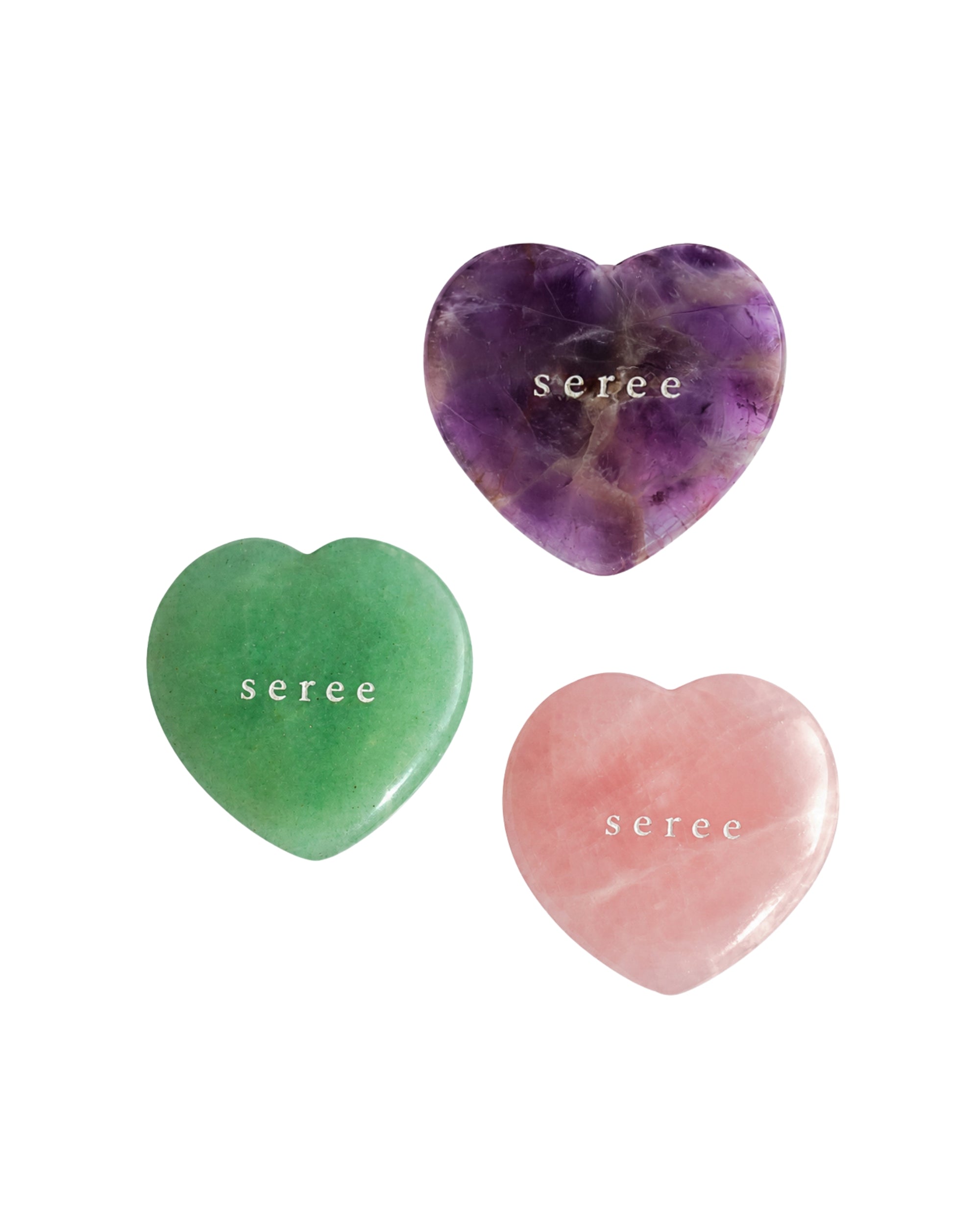 Three polished heart-shaped crystal stones on a white background: a purple amethyst, a green jade, and a pink rose quartz, each engraved with the name 'seree'.