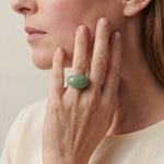 Close-up of a person wearing a green stone ring on a neutral background