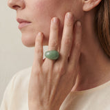 Close-up of a person wearing a green stone ring on a neutral background
