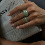 Hand with two green rings holding a newspaper