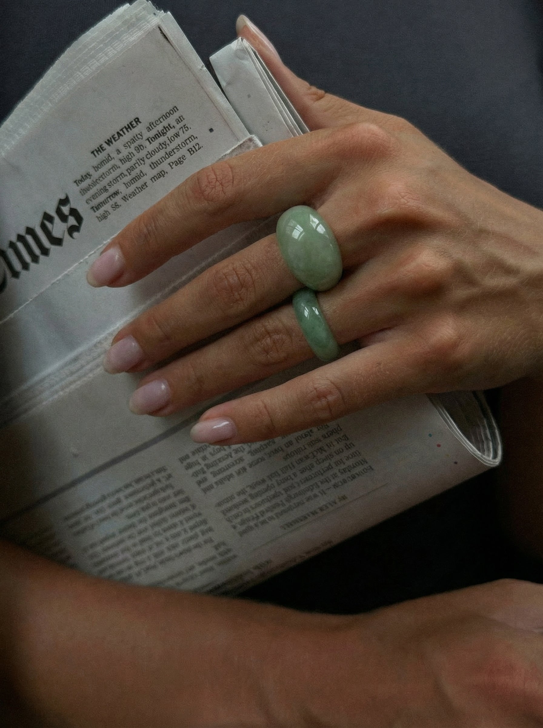 Hand with two green rings holding a newspaper