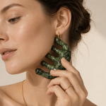 Woman using a green jade skin tool on face on a beige background