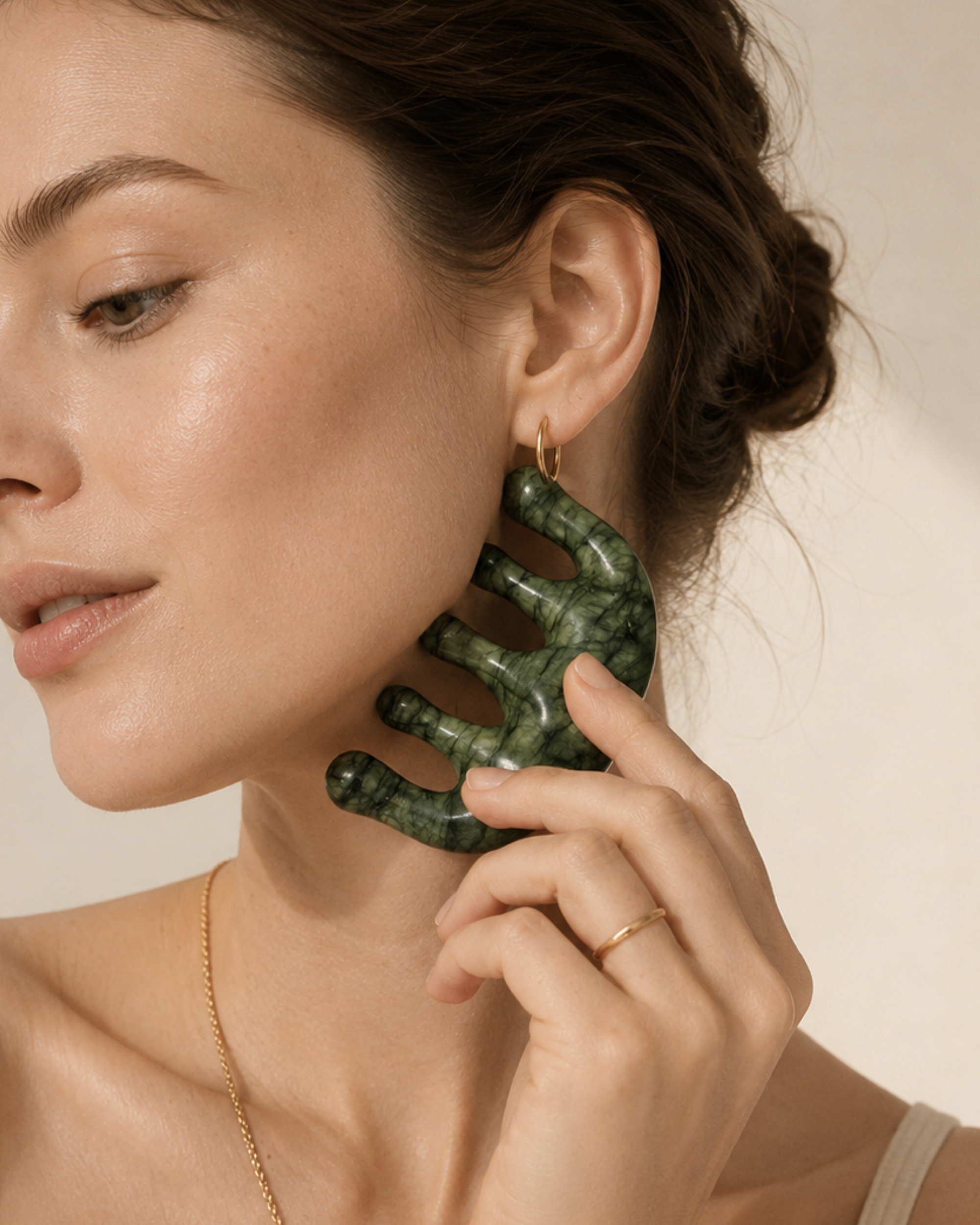 Woman using a green jade skin tool on face on a beige background