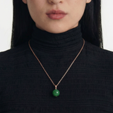 Person wearing a black turtleneck with a green spherical jade pendant necklace, close up