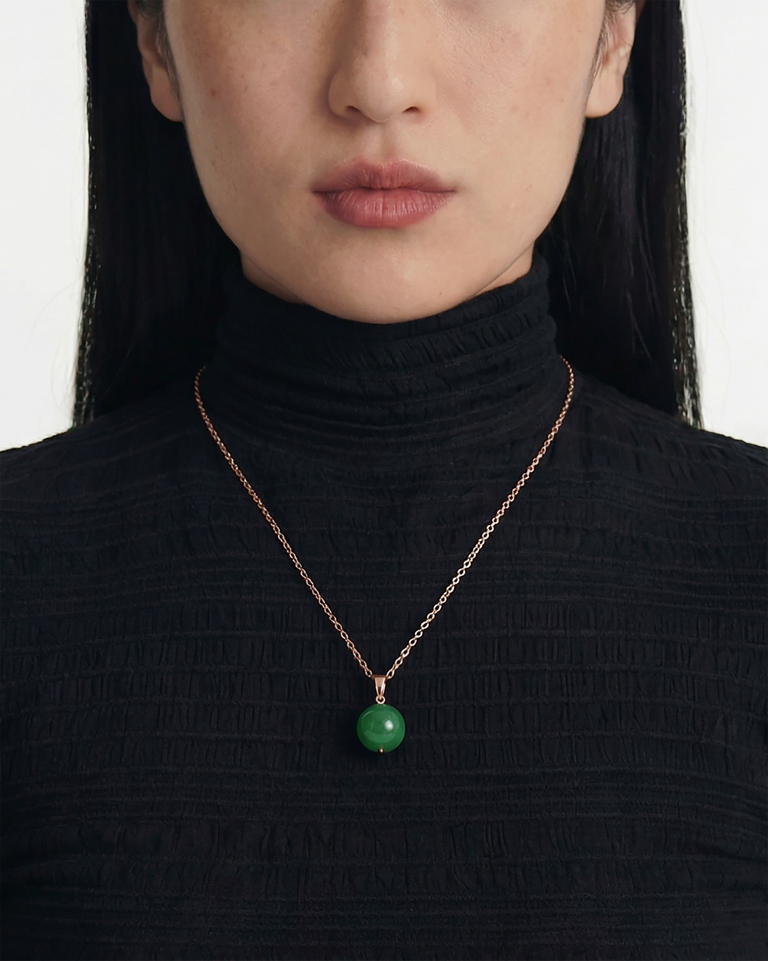 Person wearing a black turtleneck with a green spherical jade pendant necklace, close up