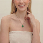 Smiling woman wearing a green spherical jade pendant necklace on a plain background, close up