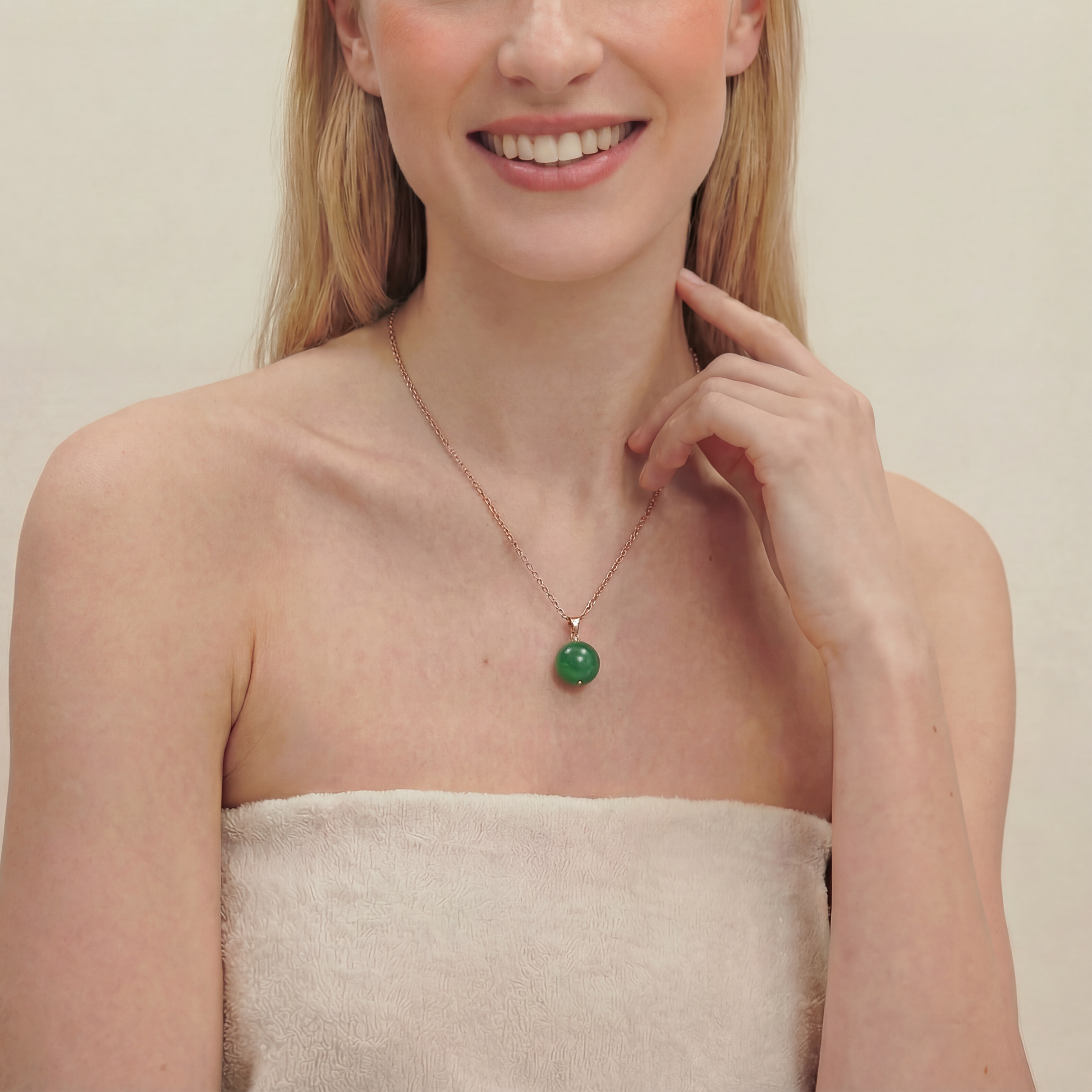 Smiling woman wearing a green spherical jade pendant necklace on a plain background, close up