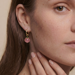 Close-up of a woman wearing a gold earring with a peach gemstone against a neutral background
