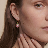 Close-up of a woman wearing a gold earring with a peach gemstone against a neutral background