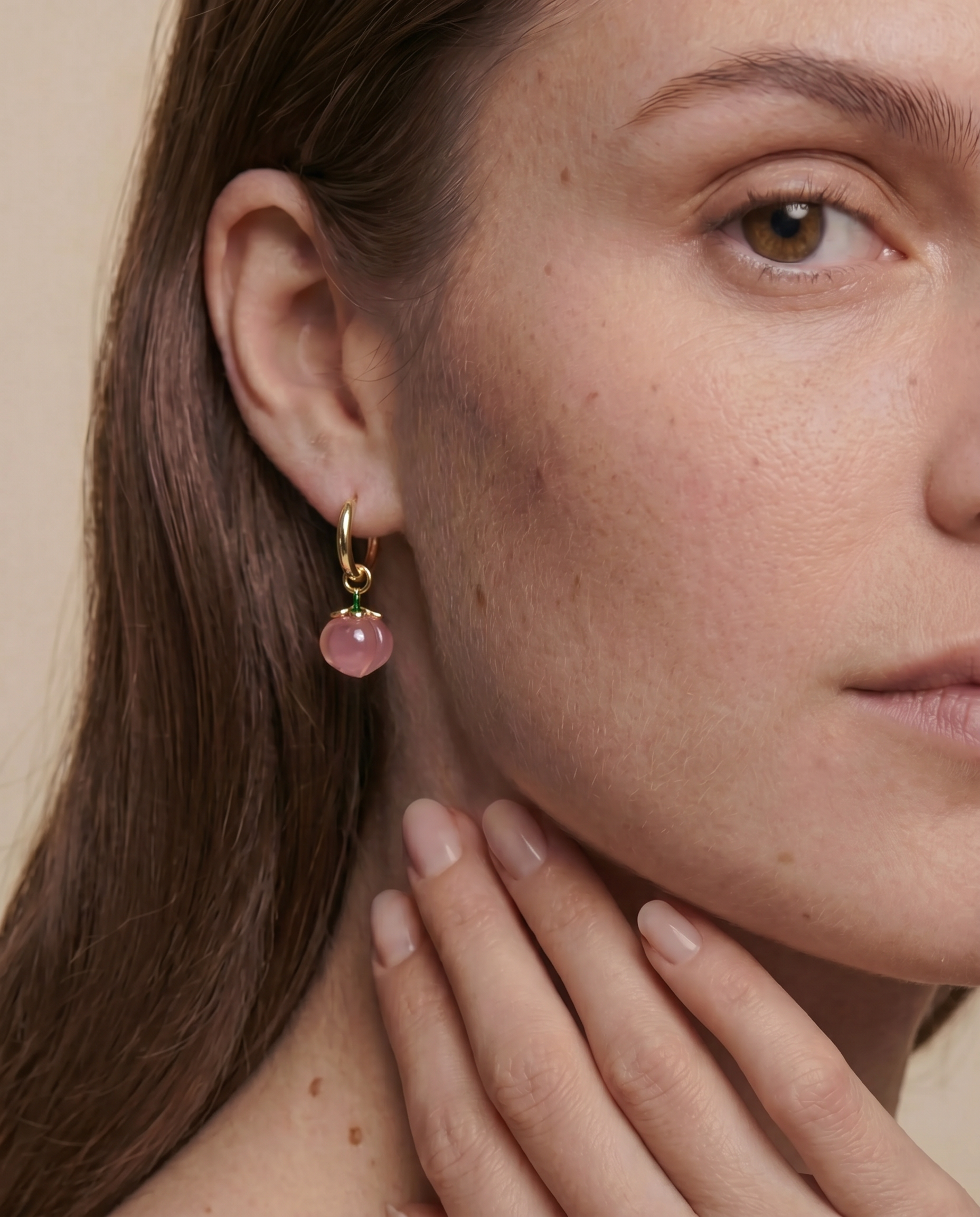 Close-up of a woman wearing a gold earring with a peach gemstone against a neutral background