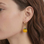 Close-up of a person wearing a pumpkin-shaped earring with a gold hoop.