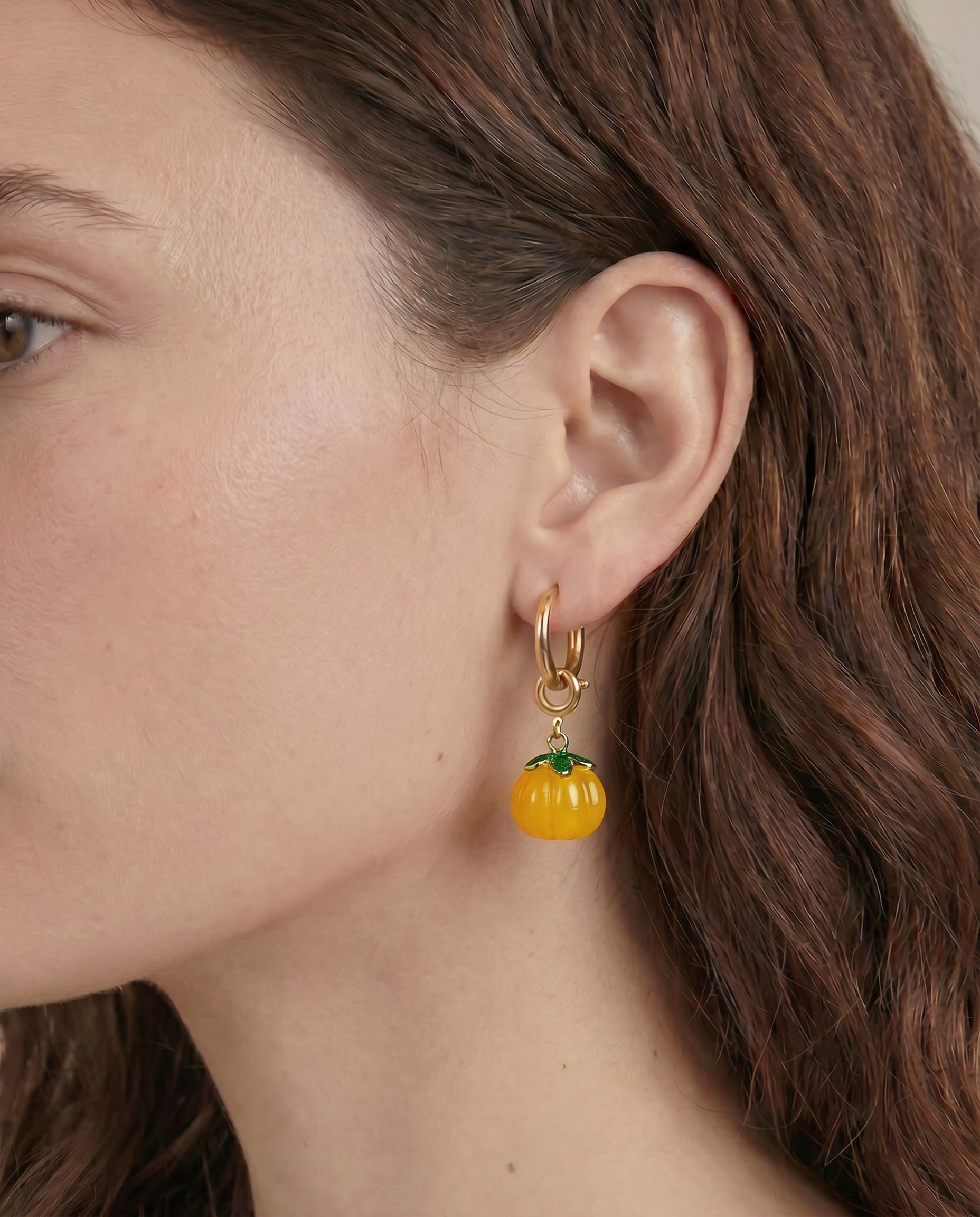 Close-up of a person wearing a pumpkin-shaped earring with a gold hoop.